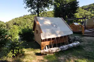Zelt auf einer Wiese am Hang mit Holzveranda, Geländer und Bäumen im Hintergrund.