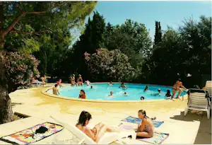 Camping-Pool mit türkisfarbenem Wasser, Sonnenliegen und mehreren Personen im Becken, umgeben von Bäumen und Liegeflächen.