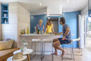 Moderne Küchenzeile mit Barhockern, drei Personen am Tresen und großen Fenstern im hellen Wohnbereich eines Campingunterkunfts.