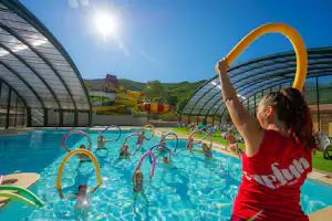 Kind im Schwimmbecken eines Campingplatzes, hält einen bunten Reifen, im Hintergrund weitere Kinder und Beckenlandschaft.