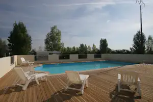 Dachterrasse mit Holzdecks, mehreren Liegestühlen und Blick auf den Pool, umgeben von Bäumen und einem Zaun.