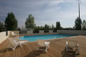 Terrasse mit Holzdeck und mehreren Liegestühlen vor einem Camping-Pool, im Hintergrund Bäume und ein Zaun.