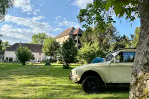 Campinggelände mit Wohnhaus, Rasenfläche und Bäumen; im Vordergrund ein gelber Oldtimer mit Zelt im Hintergrund.