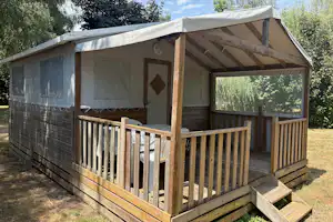 Glamping-Zelt mit Holzveranda, Vorhängen und großen Fenstern, umgeben von Bäumen im Campingbereich.