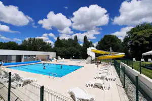 Schwimmbecken auf dem Campingplatz mit gelber Wasserrutsche, Liegestühlen und weißen Gebäuden am Rand.