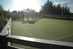 Tennisplatz auf dem Campinggelände mit Umzäunung, gepflegtem Kunstrasen und Bäumen im Hintergrund.