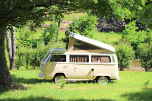 Wohnmobil mit ausklappbarem Dachzelt steht auf einer grünen Wiese zwischen Bäumen und Hecken.