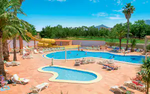 Großes Camping-Schwimmbecken mit zwei Beckenbereichen, Sonnenliegen und Sonnenschirmen am Terrassenrand, Palmen und Bäume im Hintergrund.
