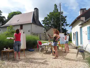 Terrasse am Camping-Ferienhaus mit Grill, Gartenmöbeln und zwei Personen vor dem Eingang, umgeben von Bäumen und Sträuchern.