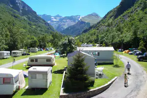 Campingplatz im Tal mit Wohnwagen und Wohnmobilen auf Stellplätzen, Kiesweg und Blick auf Berge und Gletscher im Hintergrund.