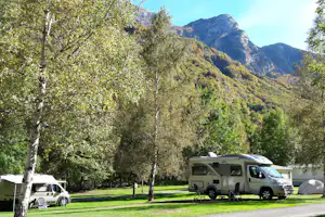 Wohnmobil und Campingbus auf einem Stellplatz im Grünen, umgeben von Bäumen und mit Blick auf die Berge.