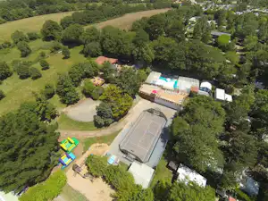 Luftaufnahme eines Campingplatzes mit Pool, großen Wiesen und mehreren Gebäuden, umgeben von Bäumen und Wegen.