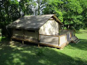 Campingunterkunft auf einer Holzplattform mit Vorbau, im Grünen zwischen Bäumen und Rasenfläche.