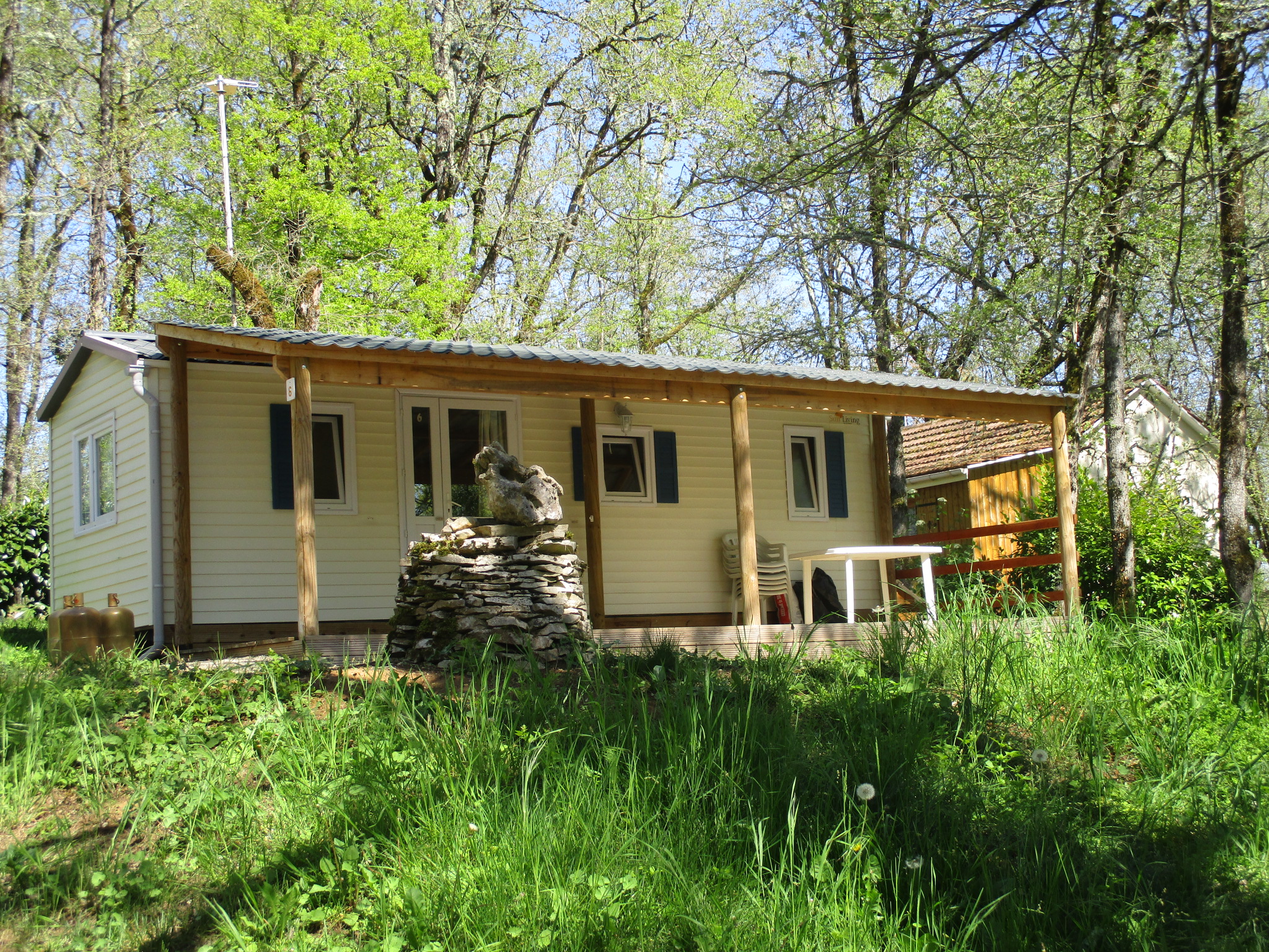 Mobilheim im Grünen mit Holzveranda und Sitzbereich, umgeben von Bäumen im Campingwald.