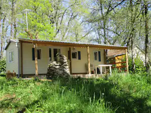 Mobilheim im Grünen mit Holzveranda und Sitzbereich, umgeben von Bäumen im Campingwald.
