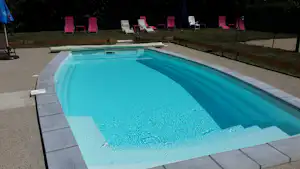Schwimmbecken auf dem Campingplatz mit türkisfarbenem Wasser, gepflasterter Umrandung und mehreren Liegen im Hintergrund.