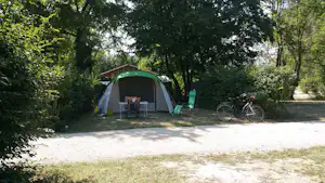 Zelt auf einem Campingplatz-Stellplatz im grünen Wald, mit Fahrrad am Rand und Tisch vor dem Eingang.