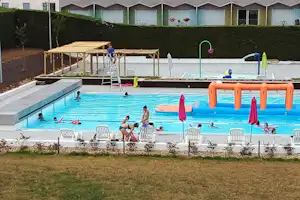Schwimmbecken im Campingbereich mit Wasserspiel, orangefarbenem Sprungbereich und Liegestühlen am Beckenrand.
