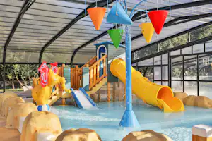 Innenbereich mit Kinder-Wasserrutschen und kleinem Pool, bunten Rutschen und Spielgeräten unter einem Glasdach.
