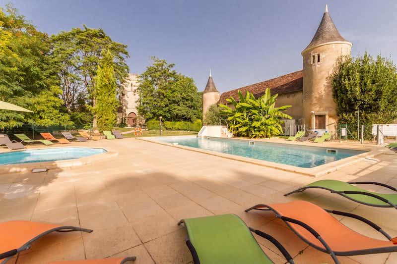Camping Le Petit Trianon de Saint-Ustre  -  Pool vom Campingplatz mit Liegestühlen in der Sonne vor einer mittelalterlichen Burg
