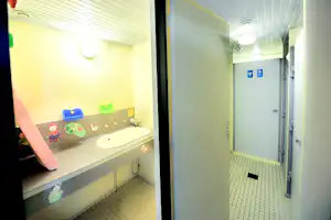 Kinderwaschbecken im hellen Camping-Badezimmer mit Fliesenboden, Wandbildern und Blick in den Flur mit Türen.