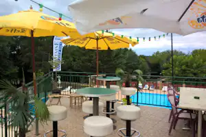 Camping Le Pigeonnier - Bar-Terrasse mit Sonnenschirmen und Pool-Ansicht