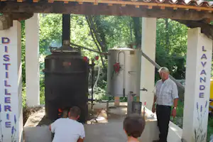 Grill und großer Kessel unter einem Holzvordach, daneben ein Mann und weitere Personen auf dem Campingplatz.