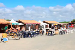 Terrasse am Campingplatz mit vielen Tischen und Stühlen, Sonnenschirmen und Fahrrädern vor den Gebäuden.