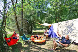 Campingplatz im Wald: Zelte, Hängematten und Schlauchboot auf dem Stellplatz zwischen Bäumen und Schatten.