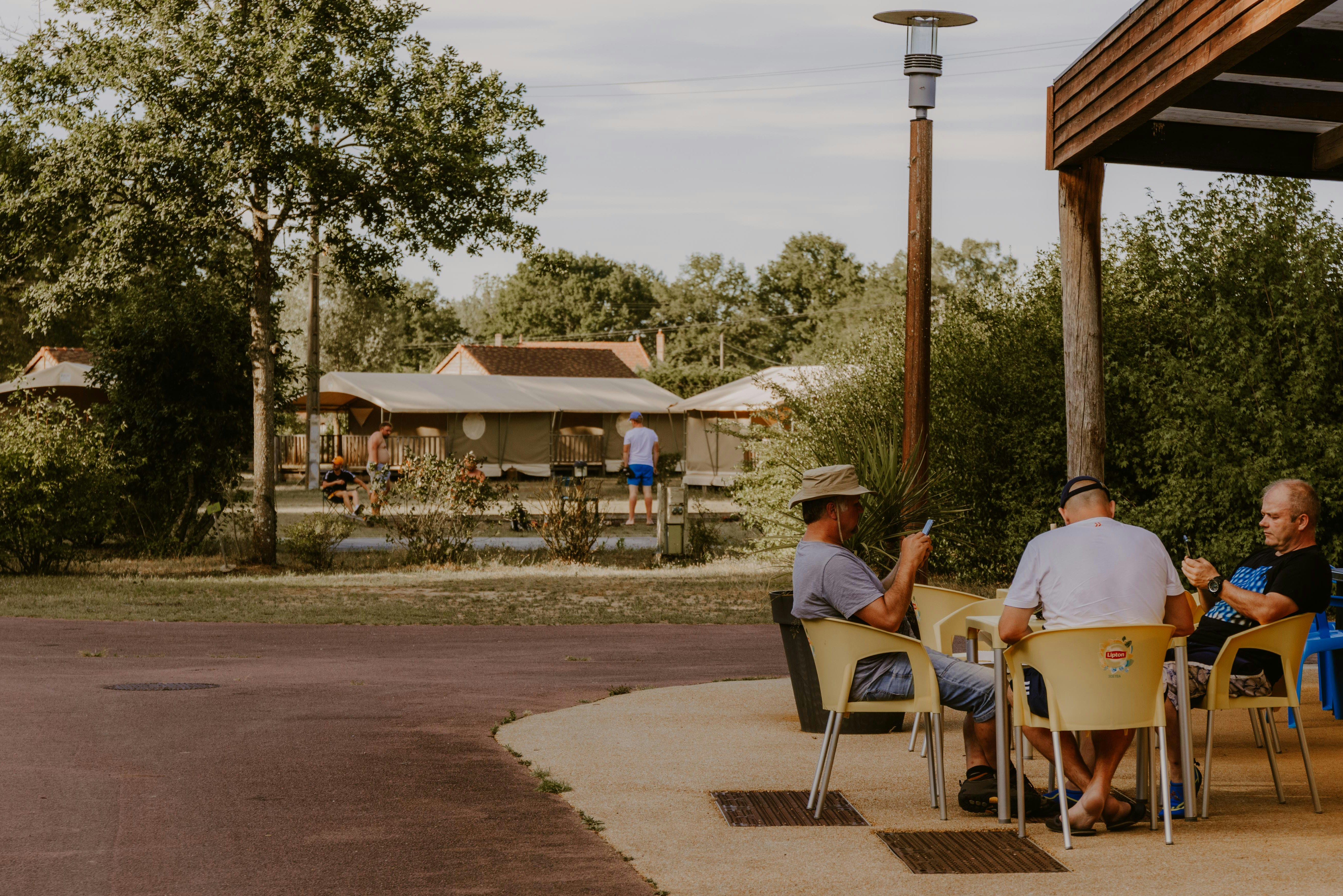 Camping Le Pont Romain - Sitzgelegenheiten außerhalb des Restaurant und Blick auf Mietunterkünfte im Hintergrund