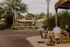 Campingplatz mit großen Zelten, Sitzbereich mit gelben Stühlen und Blick auf Bäume und Wege im Hintergrund.