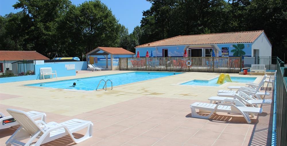 Schwimmbad mit mehreren Liegestühlen auf dem Terrassenboden, im Hintergrund Campinggebäude und Bäume.