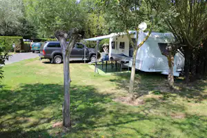 Campingzelt mit Vorzelt auf grünem Rasen, daneben Tisch und Stühle, im Hintergrund geparkter Pickup und Wohnwagen.