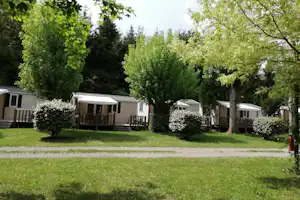 Reihe von Mobilheimen mit Veranda und Markise auf einem Campingplatz, umgeben von Bäumen und Rasen.