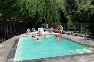 Camping-Pool mit türkisfarbenem Wasser, Steinplatten-Terrasse, Gartenzaun und vielen Bäumen im Hintergrund.