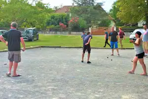 Boule-Spiel auf dem Campingplatz: mehrere Personen stehen auf der Bahn, im Hintergrund Rasen, Autos und Bäume.