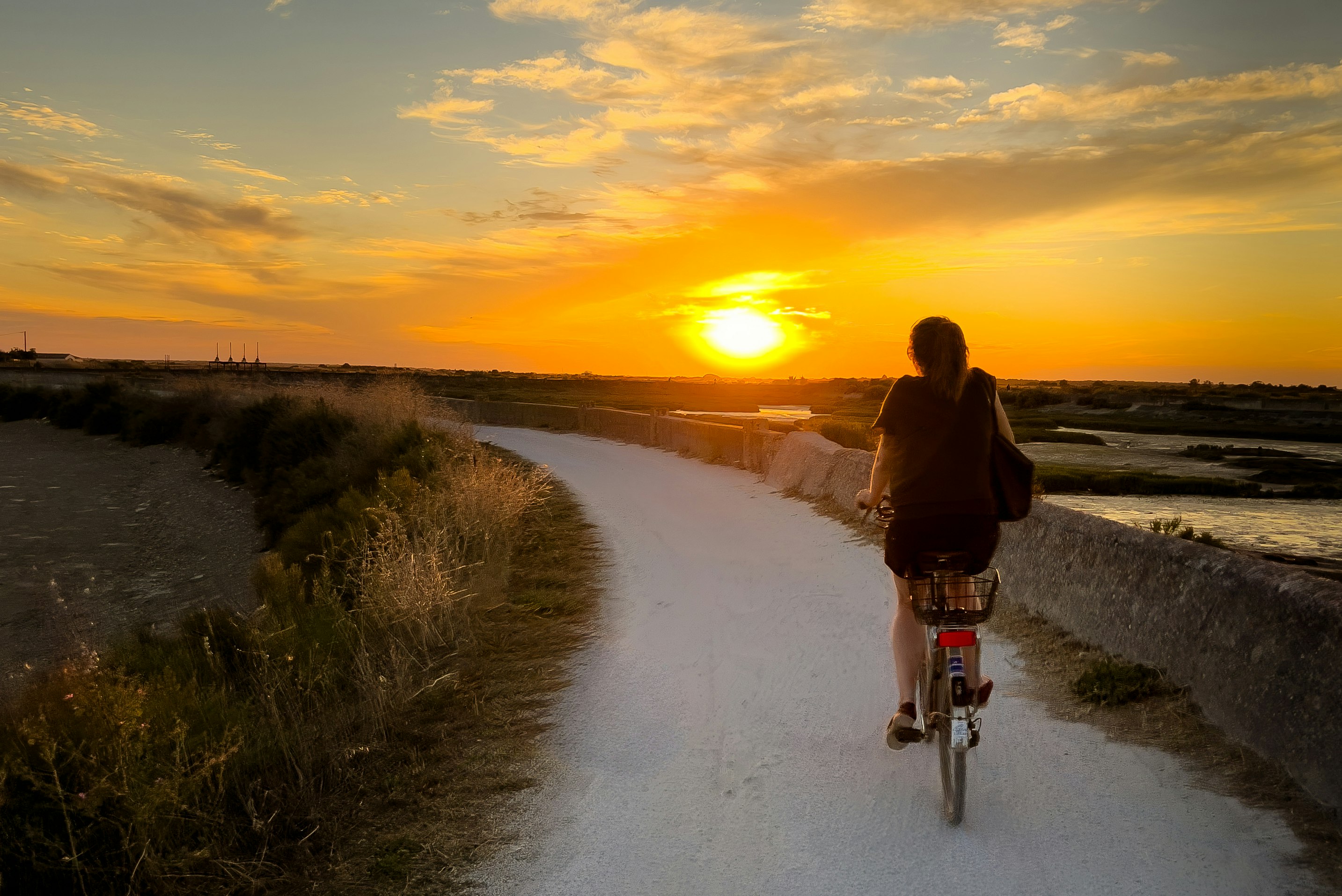 Camping Le Puma - Camperin fährt Fahrrad auf den umliegenden Fahrradwegen bei Sonnenuntergang