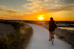 Camping Le Puma - Camperin fährt Fahrrad auf den umliegenden Fahrradwegen bei Sonnenuntergang