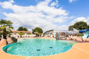 Rundes Schwimmbecken mit türkisfarbenem Wasser, daneben ein überdachter Bereich und Liegen am Campingplatz.