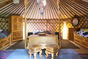 Innenansicht einer Jurte mit Bett, Holzschrank, Laternen und Traumfänger an den Wänden, dekoriert mit Teppichen.