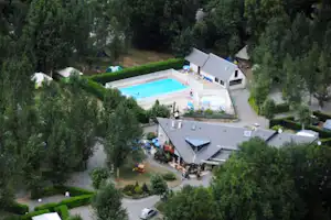 Luftaufnahme eines Campingplatzes mit Pool, Wohngebäuden und Wegen, umgeben von Bäumen und gepflegten Grünflächen.