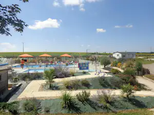 Schwimmbad mit Liegen und Sonnenschirmen, gepflegter Garten mit Wegen und Beeten sowie ein Gebäude im Hintergrund.