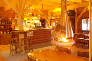 Innenansicht einer Holzbar mit Kaminfeuer, Theke mit Getränken und Sitzgelegenheiten in einer gemütlichen Hütte.