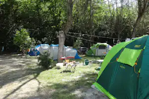 Grüne und blaue Zelte auf einem Campingplatz zwischen Bäumen, mit Campingstühlen und einem Tisch auf dem Stellplatz.