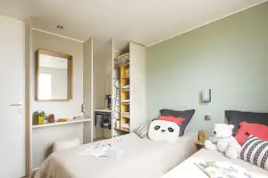 Schlafzimmer mit Doppelbett, offenen Regalen und Kissen, daneben ein Waschtisch mit Spiegel und Fenster.