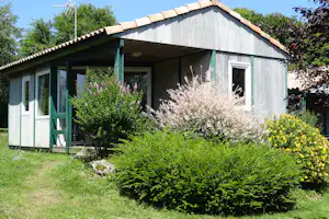 Ferienhaus mit Veranda, großen Fenstern und gepflegtem Garten mit Sträuchern und Blumen vor dem Gebäude.