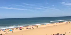 Weitläufiger Sandstrand mit vielen Sonnenschirmen, Strandzelten und Menschen am Ufer, Blick auf das Meer und die Wellen.