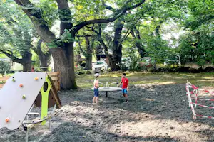 Spielplatz auf dem Campingplatz mit Kletterwand, Seilen und zwei Kindern zwischen großen Bäumen.
