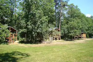 Holzterrassen und kleine Veranden auf einem Campingplatz im Grünen, umgeben von Bäumen und Rasenfläche.