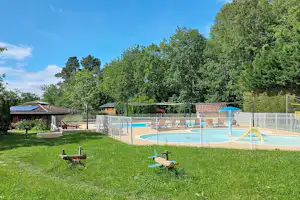 Schwimmbecken mit Umzäunung und Liegen im Garten, daneben Rasenfläche, Bäume und ein kleines Gebäude am Campingplatz.